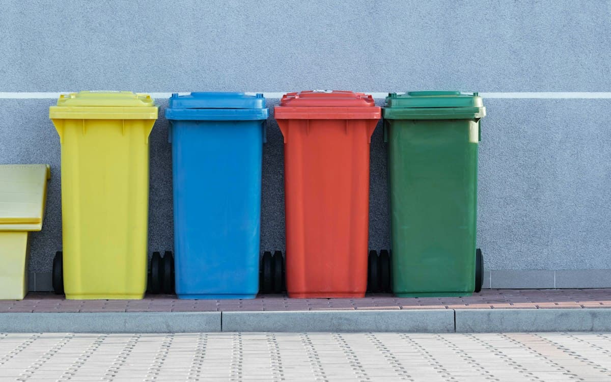 Four colour-coded waste bins lined up against a wall
